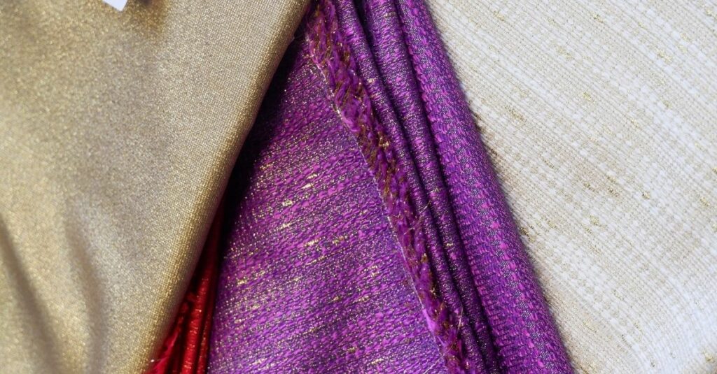 Dettaglio di tessuti sacri viola con inserti dorati, fibre naturali pregiate e lavorazioni artigianali per paramenti liturgici.